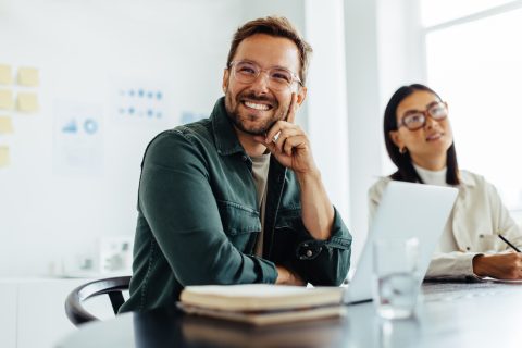 Business man listening to a discussion during a meeting in an office. Happy business man sitting in a boardroom with his colleagues.